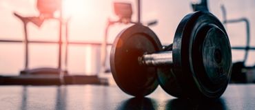 Photo of a dumbbell on a gym floor with a sunset in the background. 