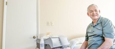 Man sits on his bed next to his home dialysis machine.