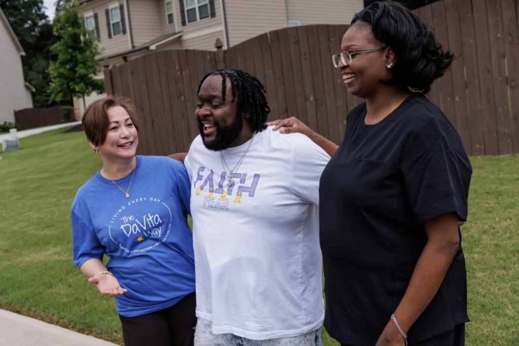 A DaVita patient stands with two DaVita teammates outside.