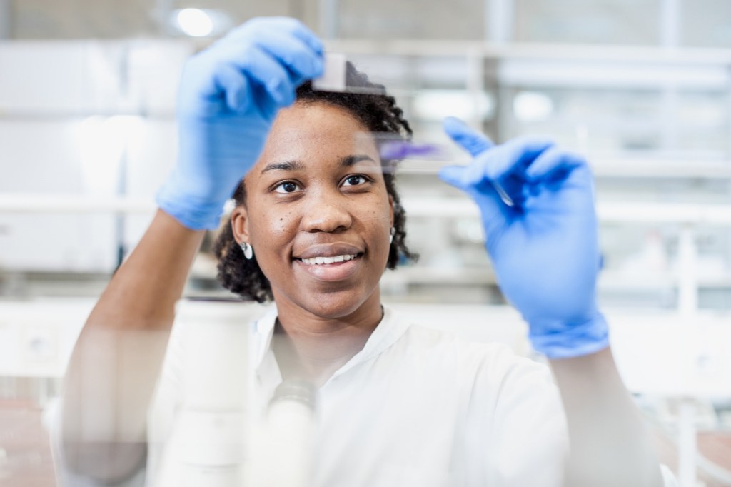 A woman wears clinical gloves as she evaluates two testing slides for medical-associated results in a lab setting.